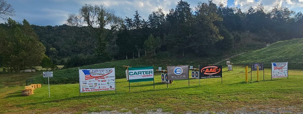 Photo of Sponsor signs in front of the Cedar Lakes Archery course with mountains in the background.